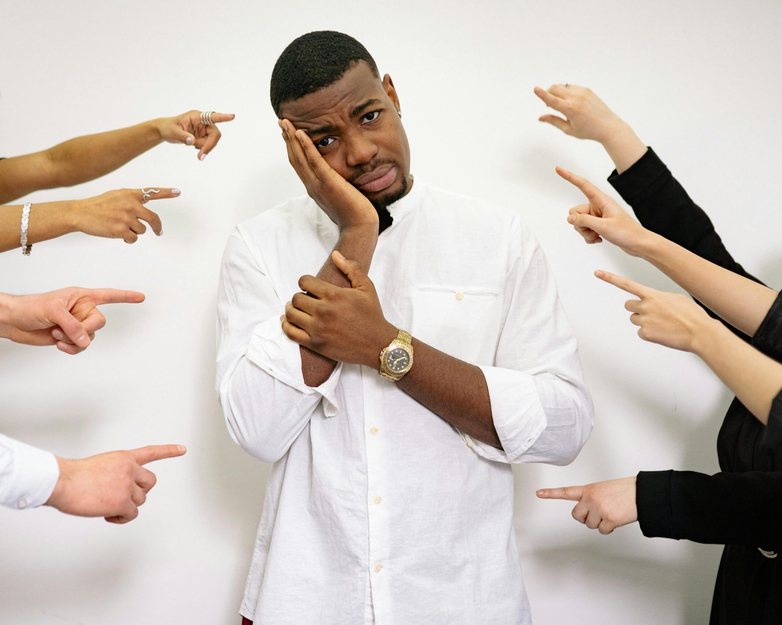 A man in a white shirt looking stressed, surrounded by hands pointing at him.